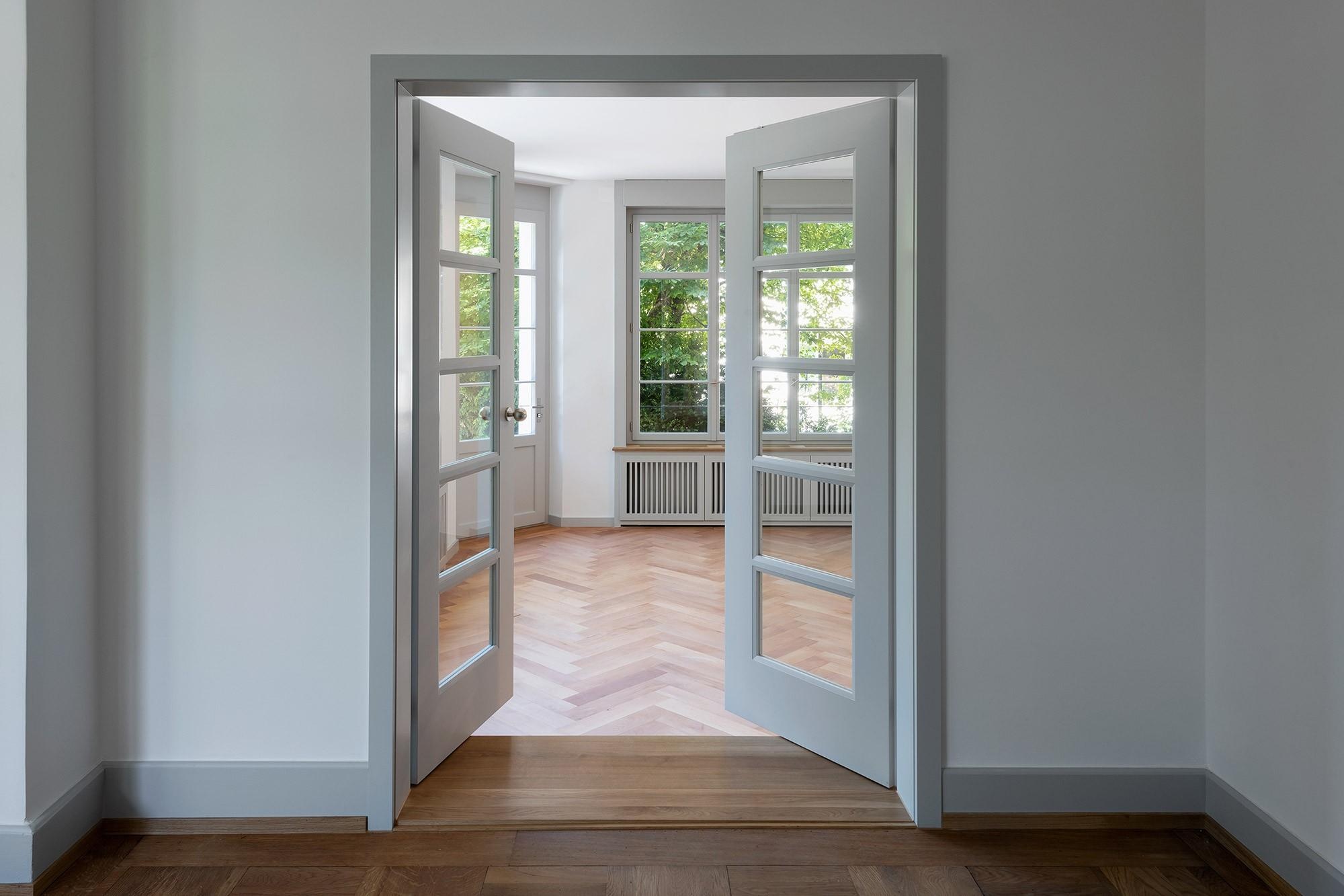 Open double doors framing a bright, empty room with herringbone parquet.