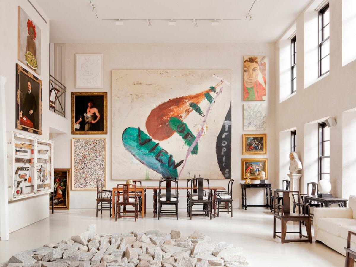 A double-height room hung with paintings above a long refectory table.