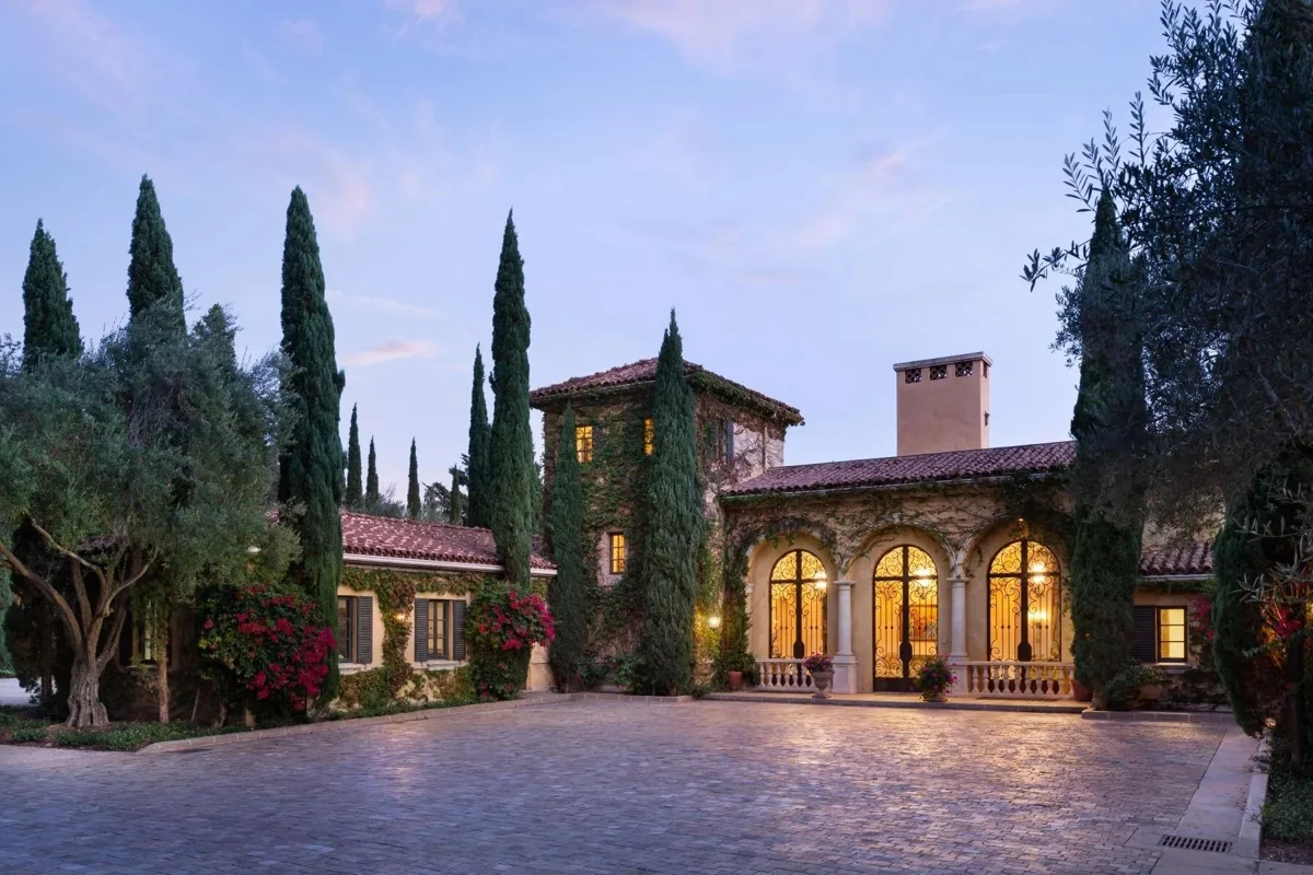 An illuminated Mediterranean villa with arched doors framed by cypress trees.