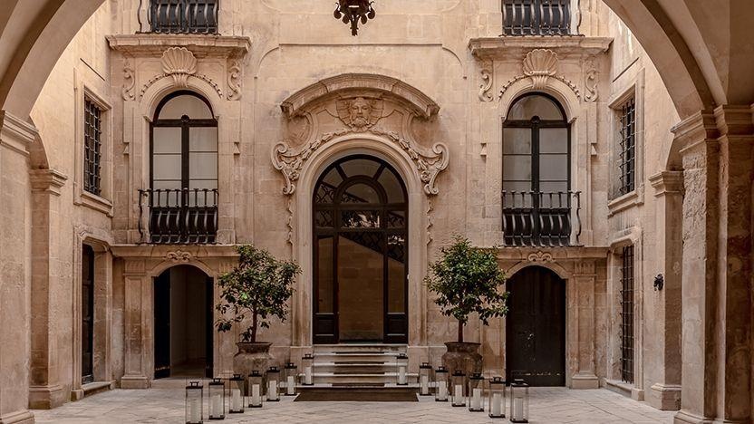 The arcaded internal courtyard of a stone palace with potted trees.