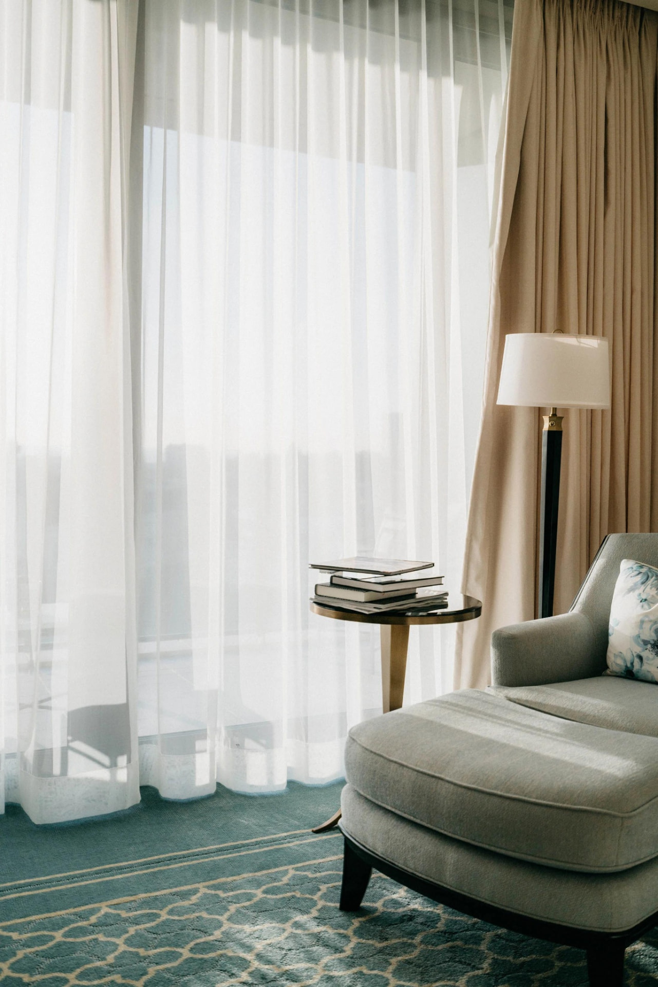 A chaise longue in a light-filled corner beside a curtained window.