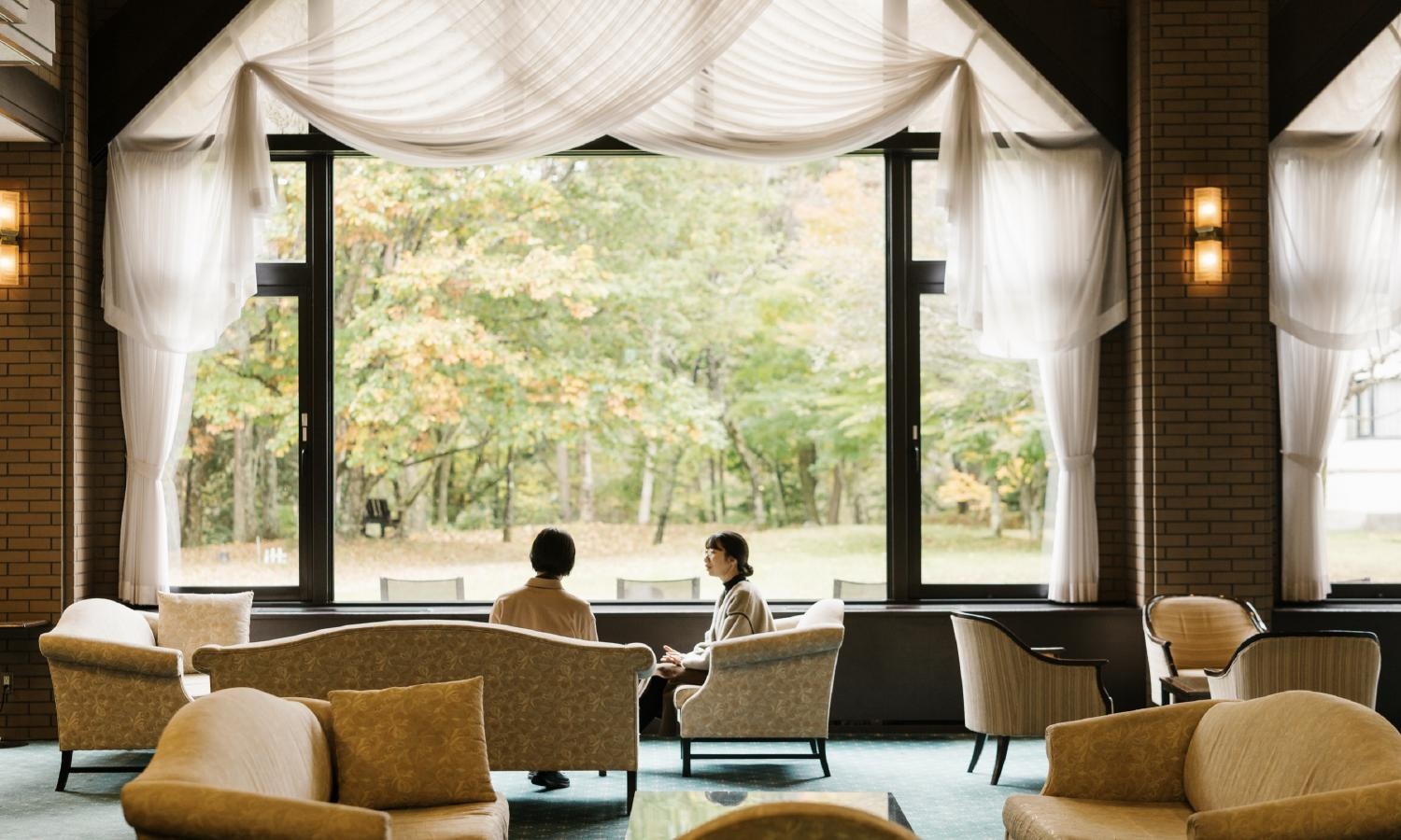 Two people in conversation in a quiet lounge overlooking woodland.