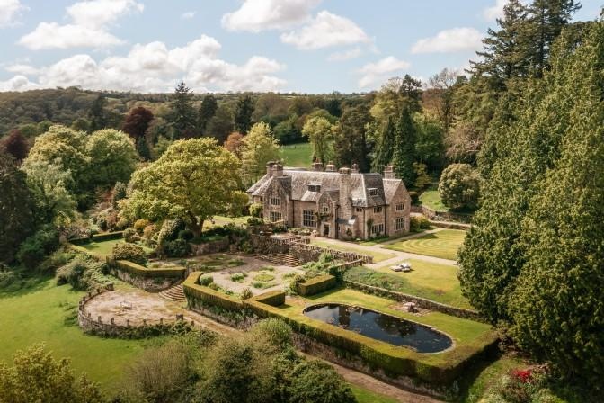 An aerial view of a stone country house set within terraced gardens.