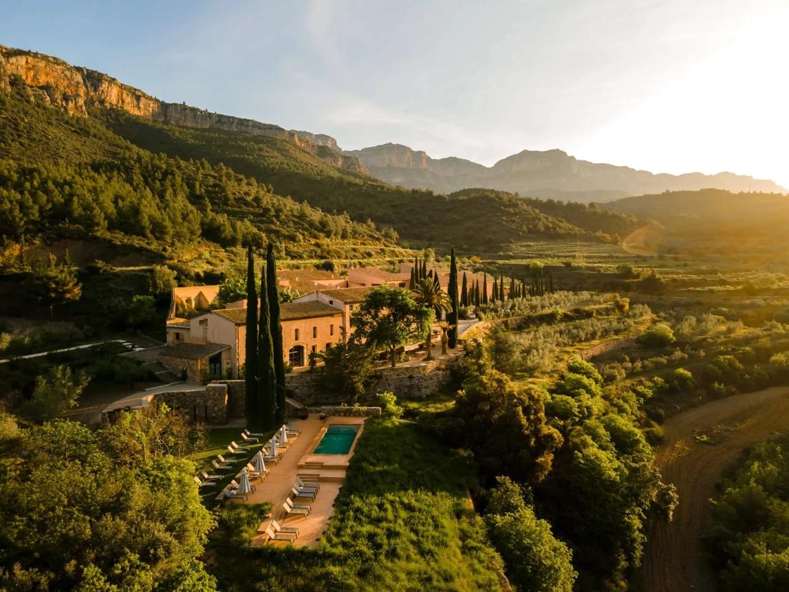 A restored stone estate in a valley of vineyards and olive terraces at sunset.