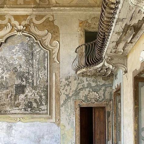 A weathered interior wall with faded frescoes beside an ornate balcony.
